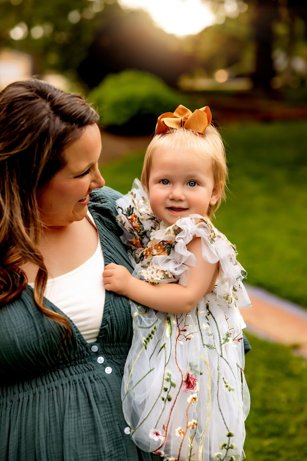 Parent and toddler share tender outdoor moments in a grassy field during golden hour sunset.