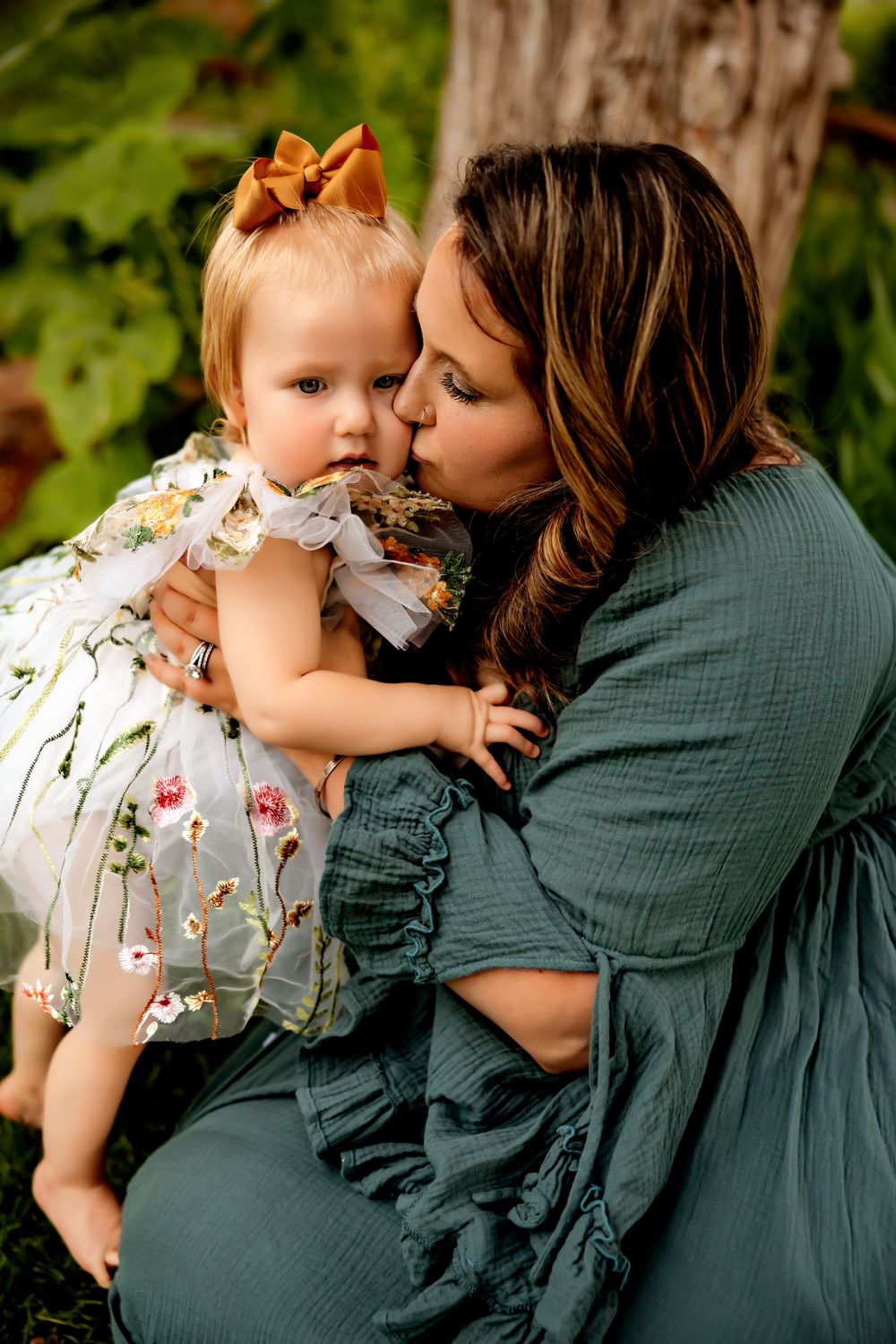 A tender moment captured outdoors showing affection between two people in green and floral outfits against a natural backdrop.