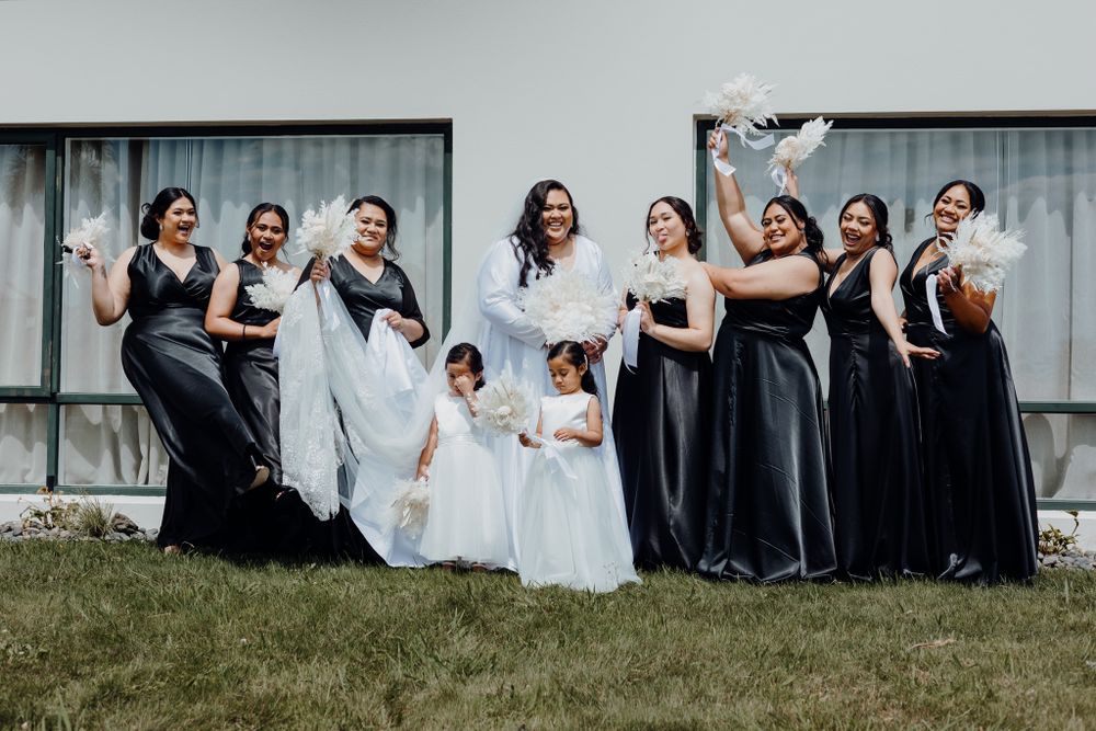 Wedding party in black dresses and white gowns poses playfully on grass.