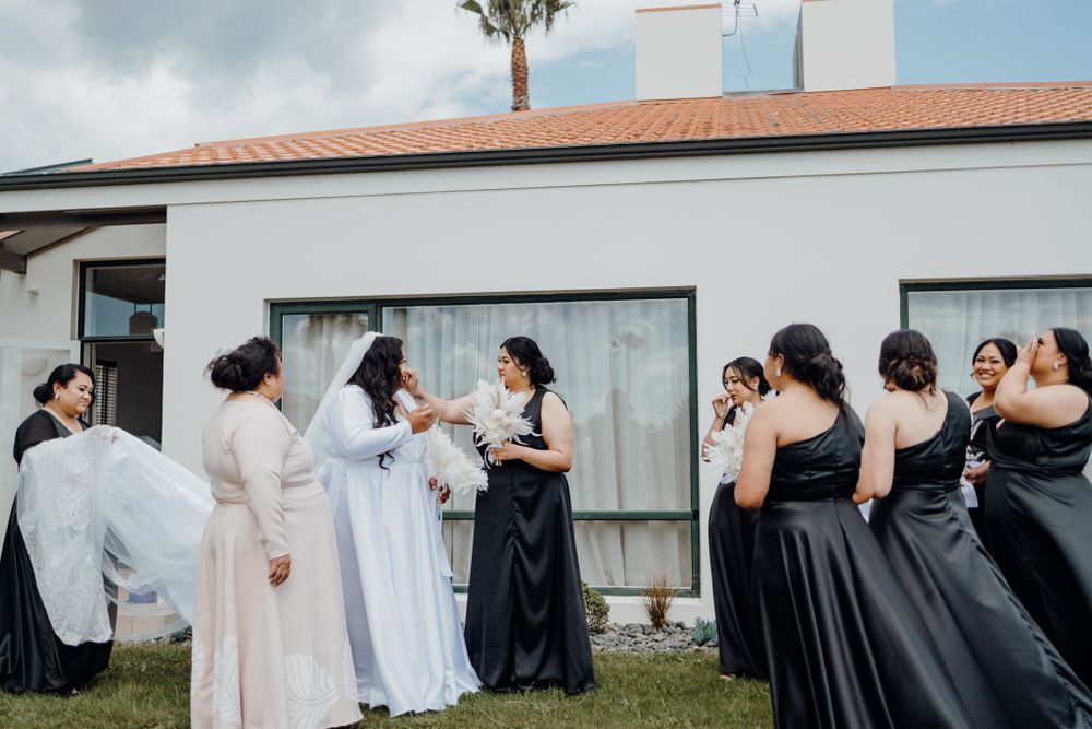 Wedding party gathers on lawn outside white building during preparation moments.