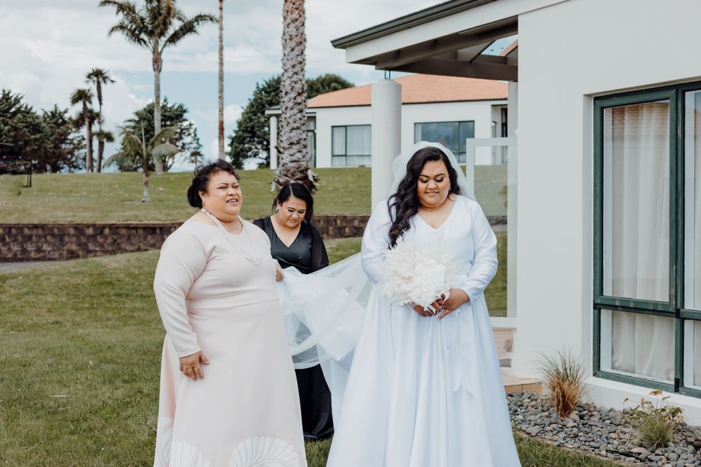 Two brides wearing beautiful white wedding dresses smile together on a grassy lawn with palm trees in the background.