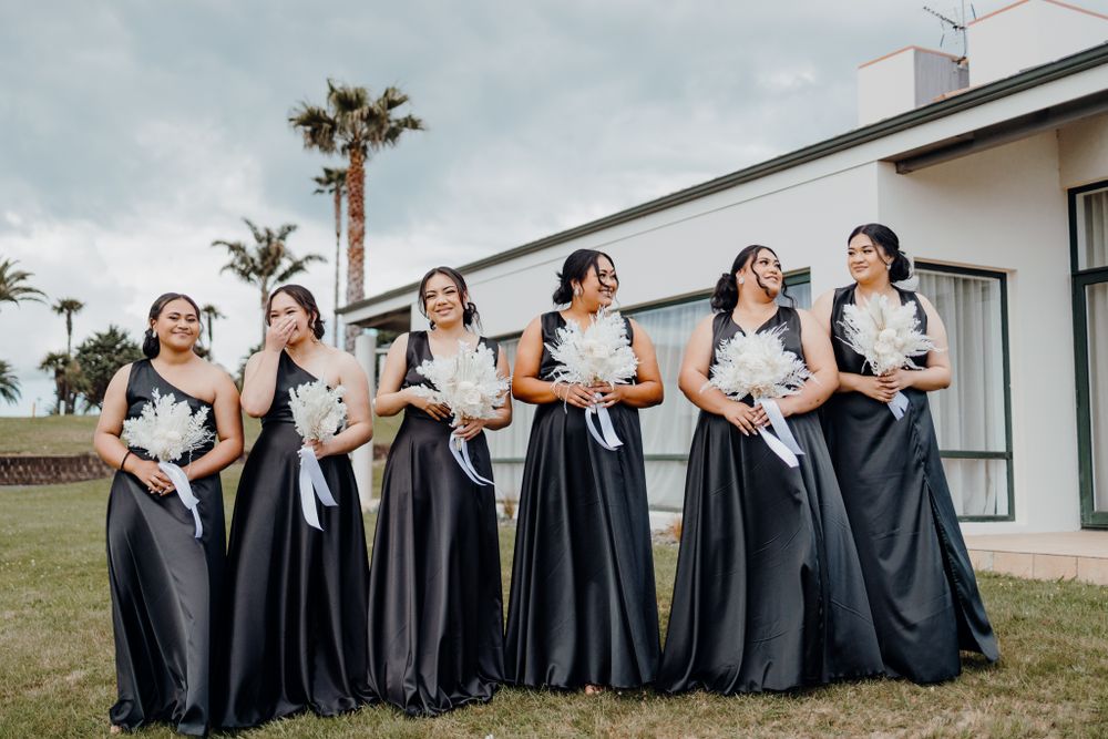 Bridesmaids in elegant black gowns pose outdoors with joyful expressions.