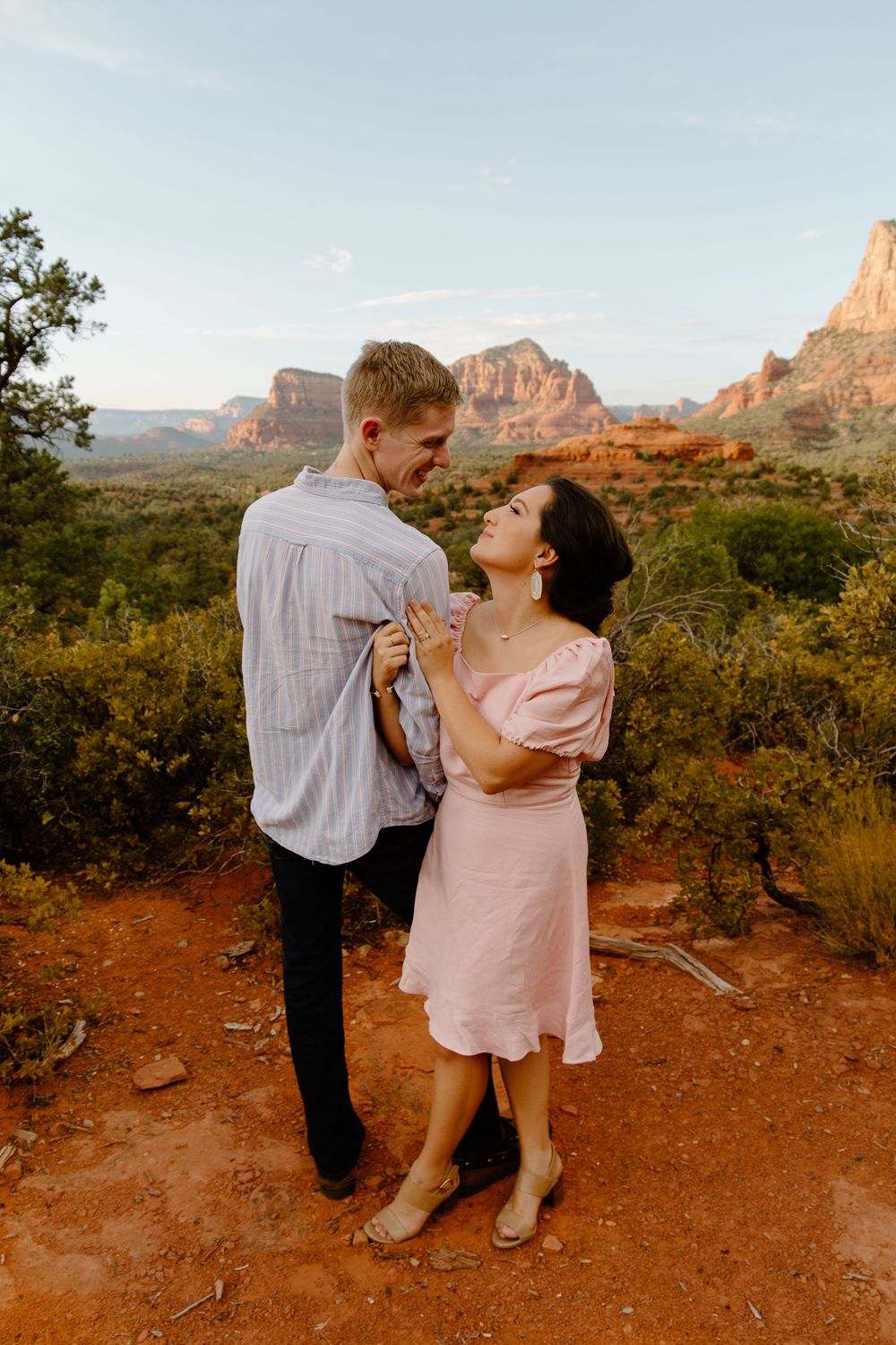 man facing towards the horizon as the woman is hugging his arm looking up at him during their Sedona engagement session