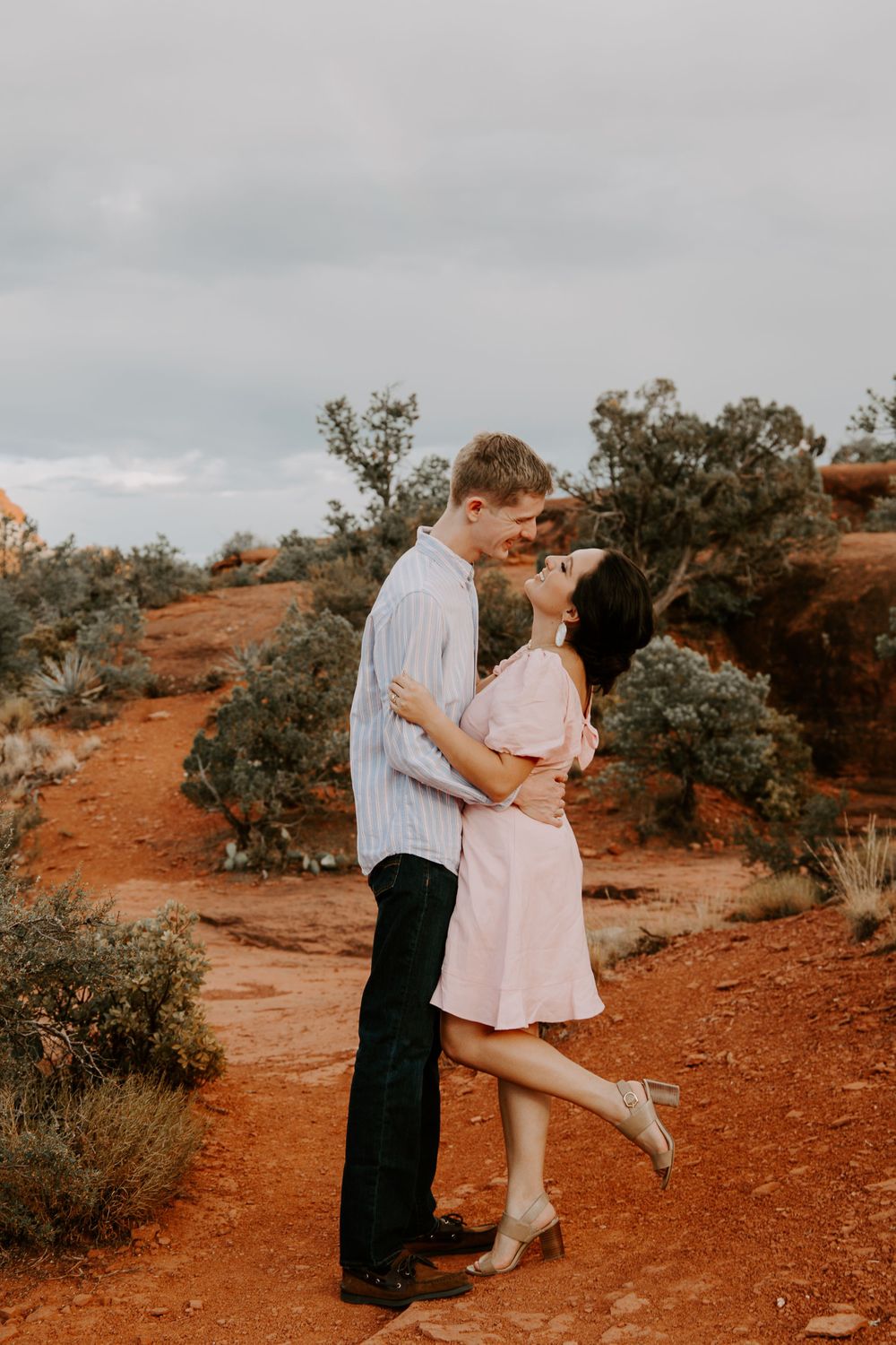 couple sharing a kiss as the woman is popping her back leg during their Bell Rock engagement shoot