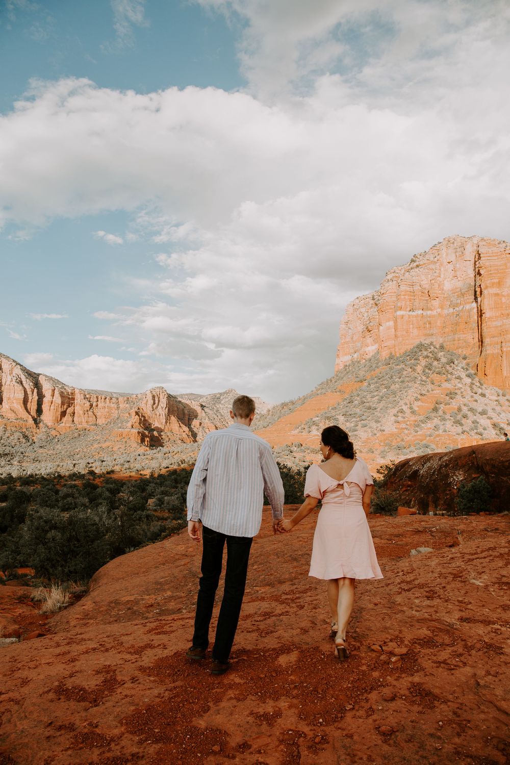 couple holding hands and walking off into the distance with the red rocks of Sedona around them