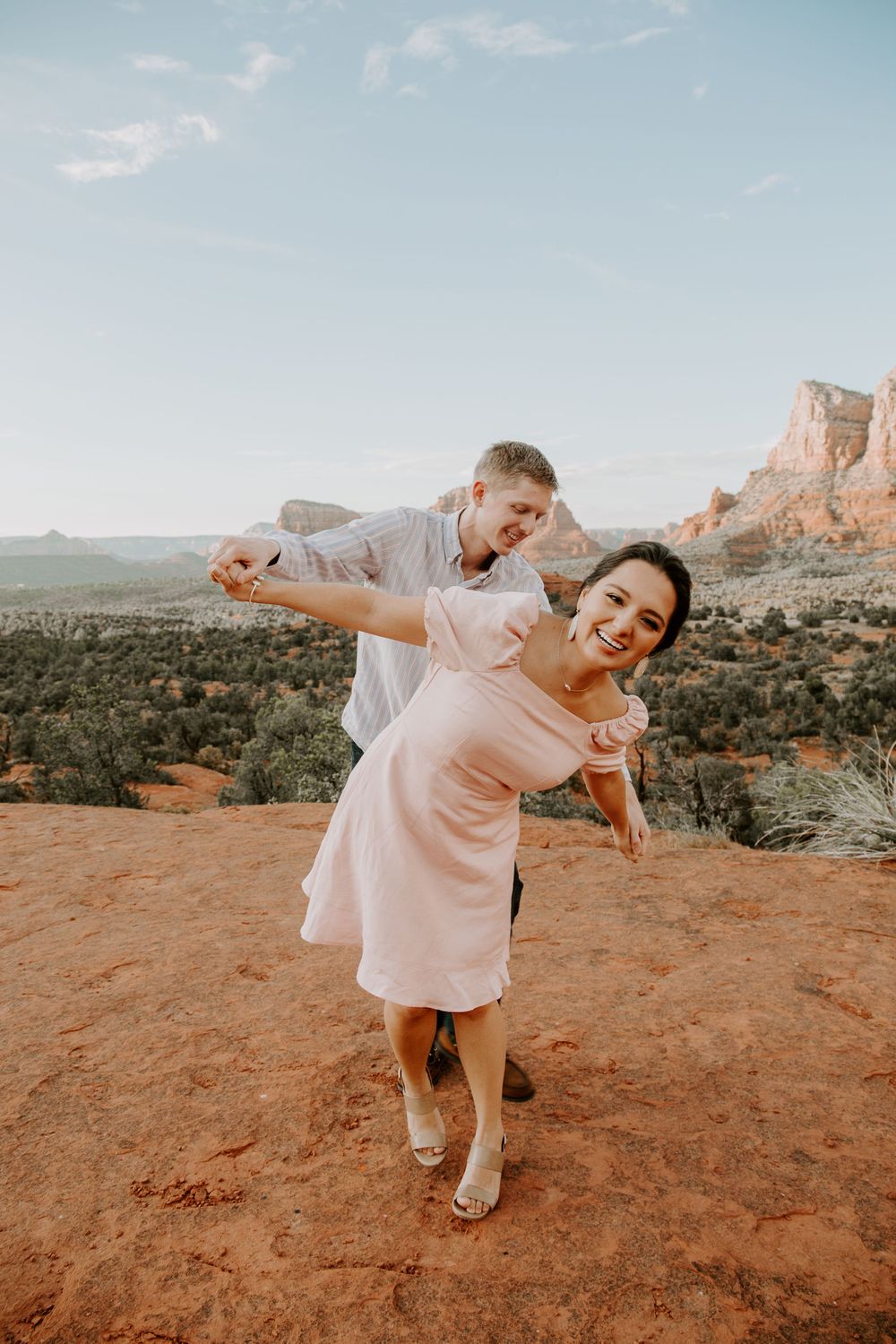 couple holding hands out to the sides of each other and acting like an airplane during their Bell Rock photoshoot