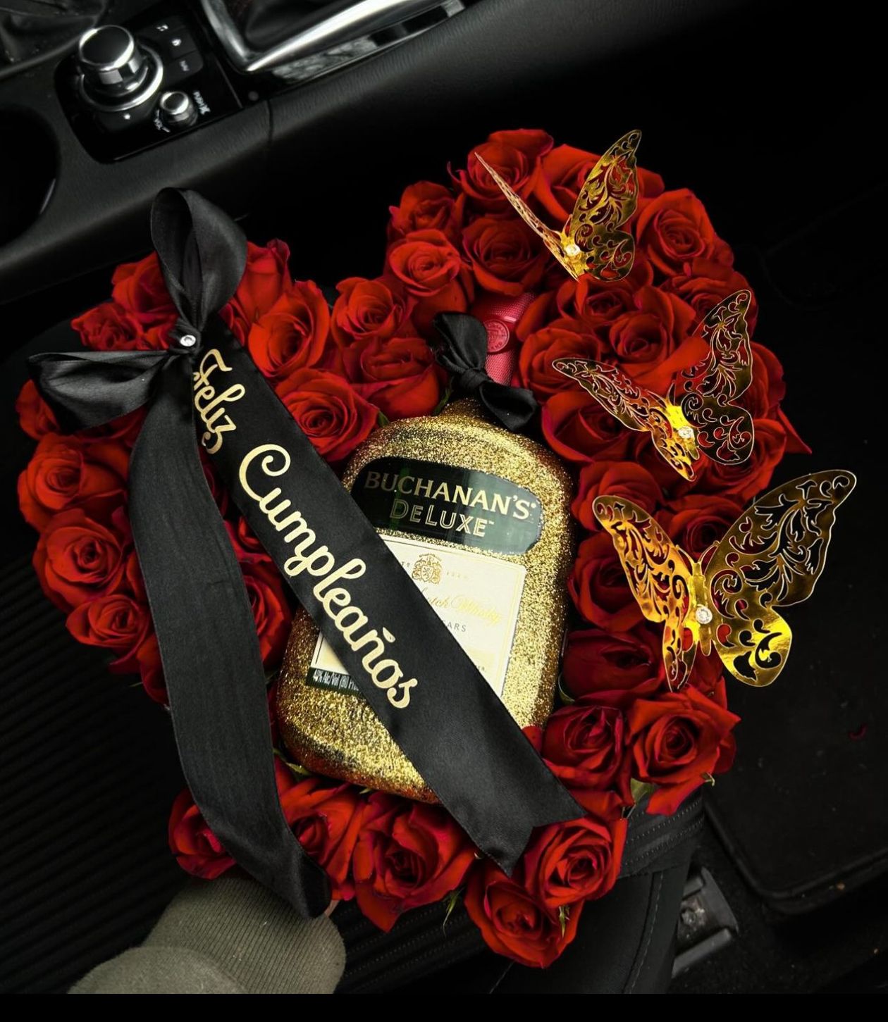 Heart-shaped arrangement of red roses with champagne bottle and gold butterflies.
