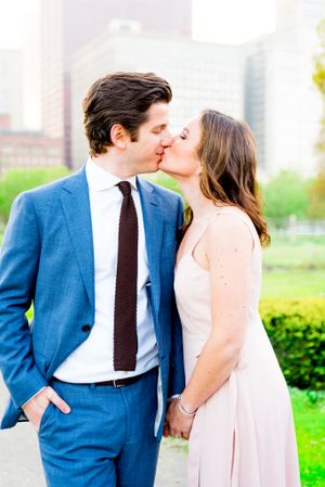 man in navy suit kissing woman in light pink dress in Grant Park for Chicago sunset engagement pictures