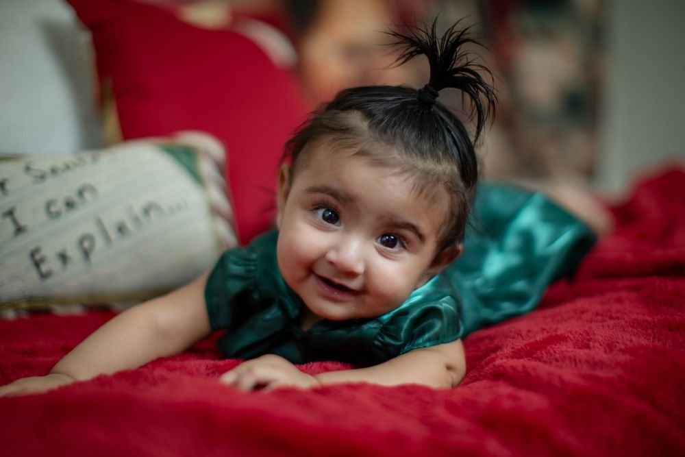 Baby in emerald green dress smiles while lying on red bedding.