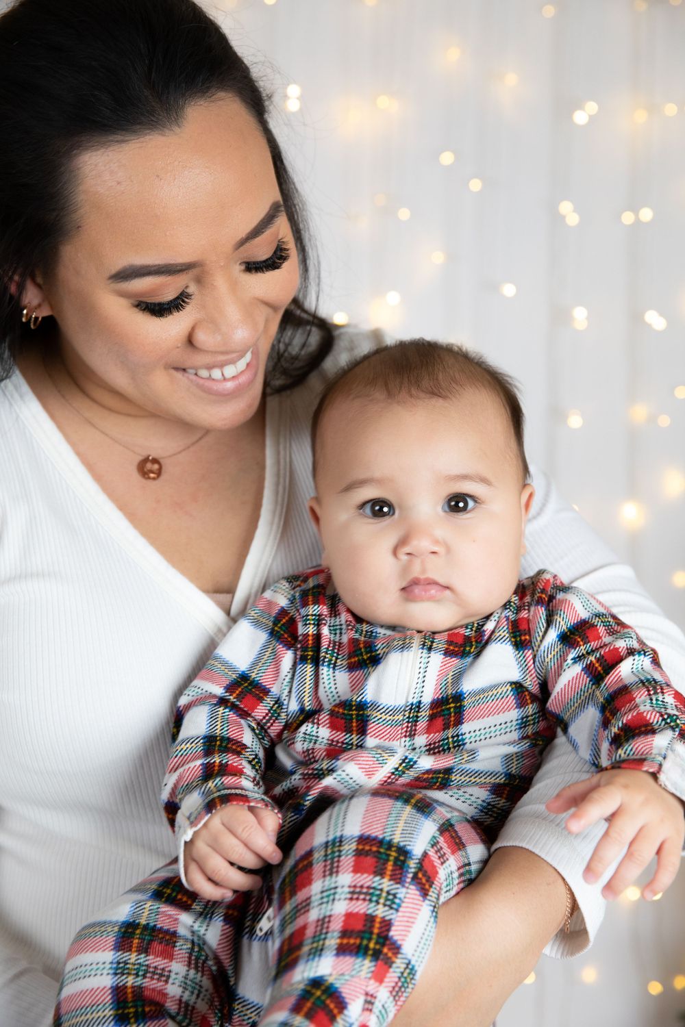 Tender moment between parent and baby in plaid Christmas outfit against sparkly backdrop.