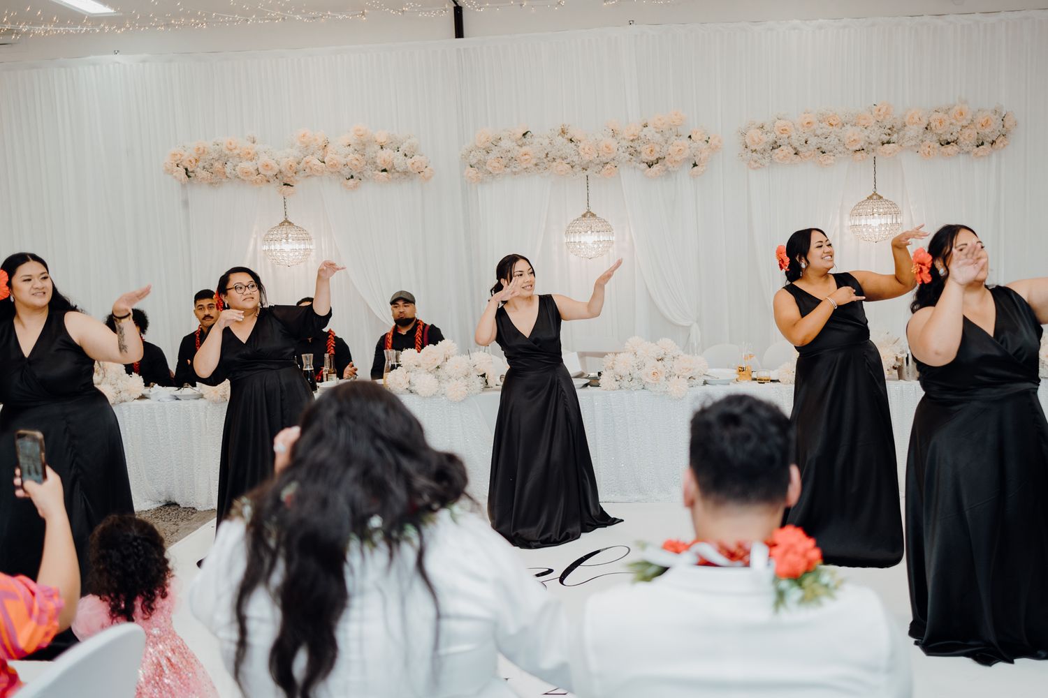 Group in black dresses performing choreographed dance at wedding reception.