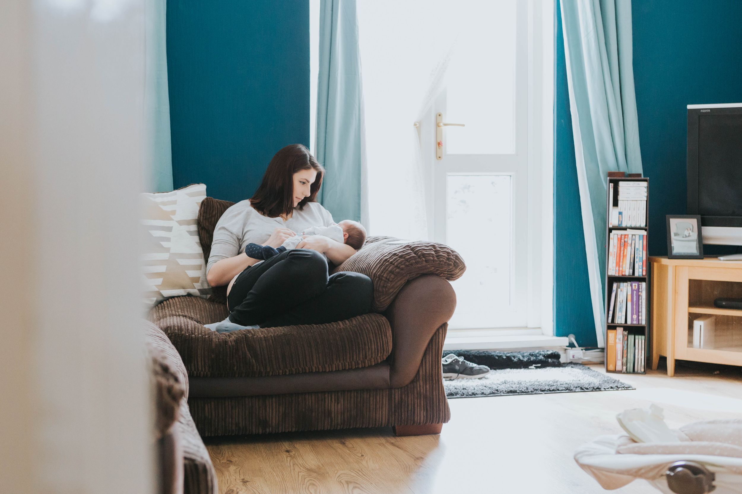 mum sitting on brown sofa in blue room looking at baby boy