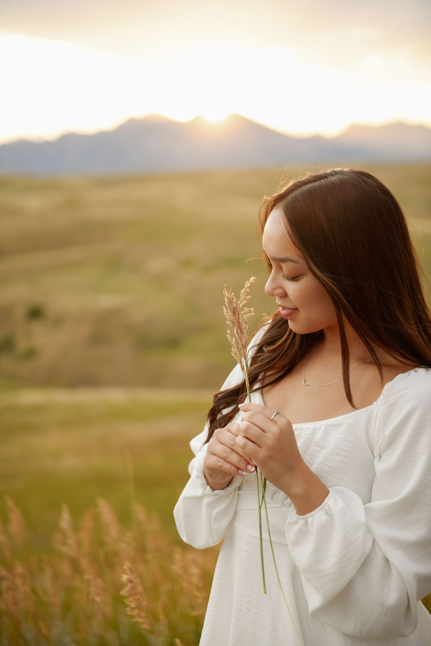 A scenic meadow at golden hour with tall grass and trees lining the background while someone poses in white attire.