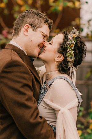 A couple shares a romantic kiss during an autumn wedding ceremony with warm brown and natural tones in the background.