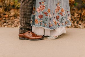 Close-up view of brown leather dress shoes and floral skirt hem with autumn leaves in background.