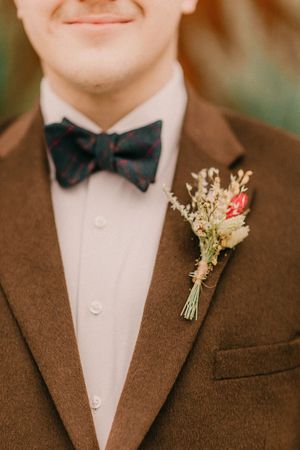 Close-up of brown suit jacket with black bow tie and delicate dried flower boutonniere in white and pink.