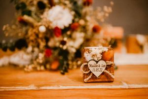 A small rustic wedding favor box with a 'thank you' tag sits on a wooden surface near blurred floral decorations.