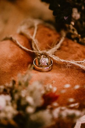 Diamond engagement ring and wedding band tied with twine on orange fabric with soft focus flowers in background.
