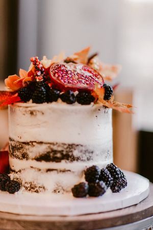 A rustic naked cake decorated with fresh blackberries and orange fall leaves on a white cake stand.