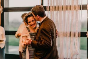 A bride and groom laugh together during an emotional wedding ceremony in front of pink drapes.