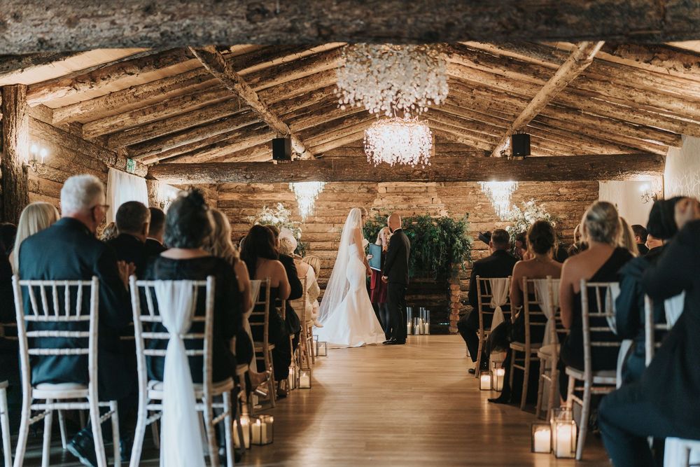 Interior of a rustic wooden barn wedding venue with crystal chandeliers and white chiavari chairs at Grand Lodge Oaklands.