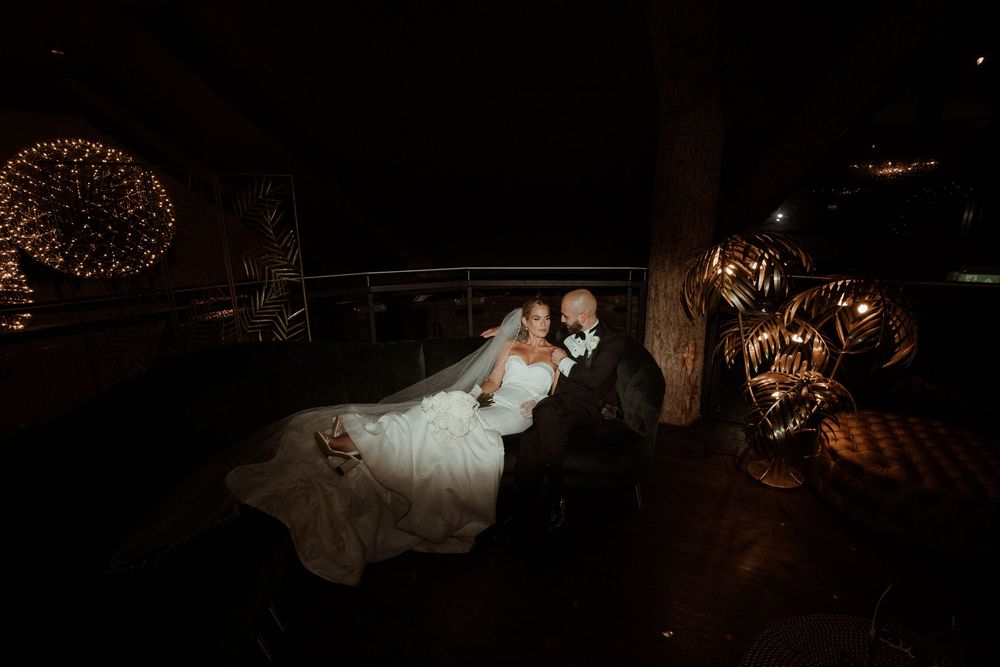 A couple in wedding attire reclines on a dark elegant couch surrounded at Grand Lodge Oaklands - taken by Grimsby photographer.