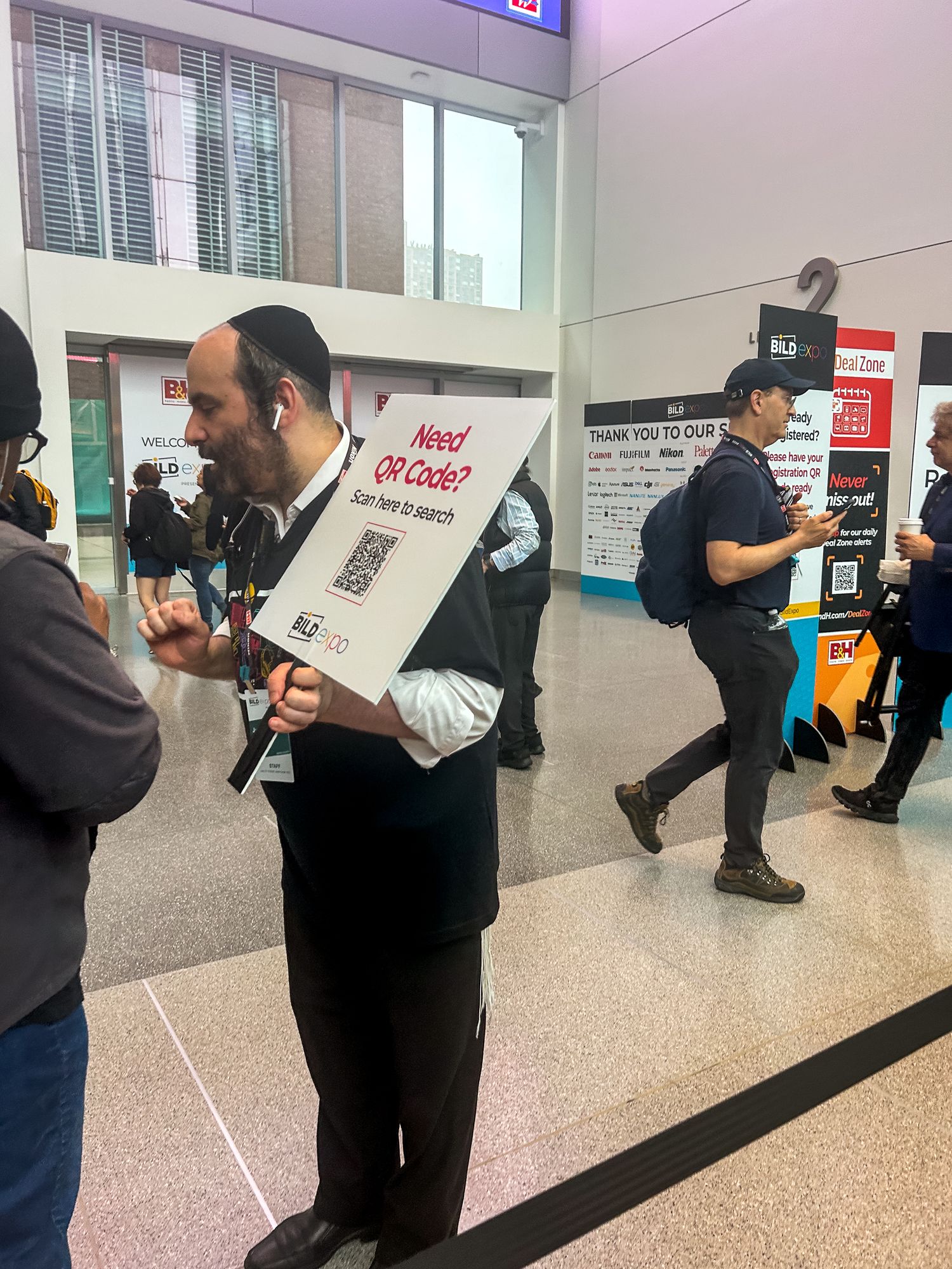 People gathered in what appears to be a lobby or hallway with someone holding a QR code sign at an event.