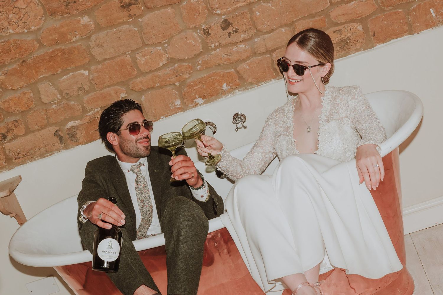 Fun photo of bride and groom drinking in bath wearing sunglasses