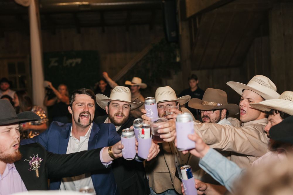 A group of people in cowboy hats toasting and celebrating with drinks at a lively indoor gathering.