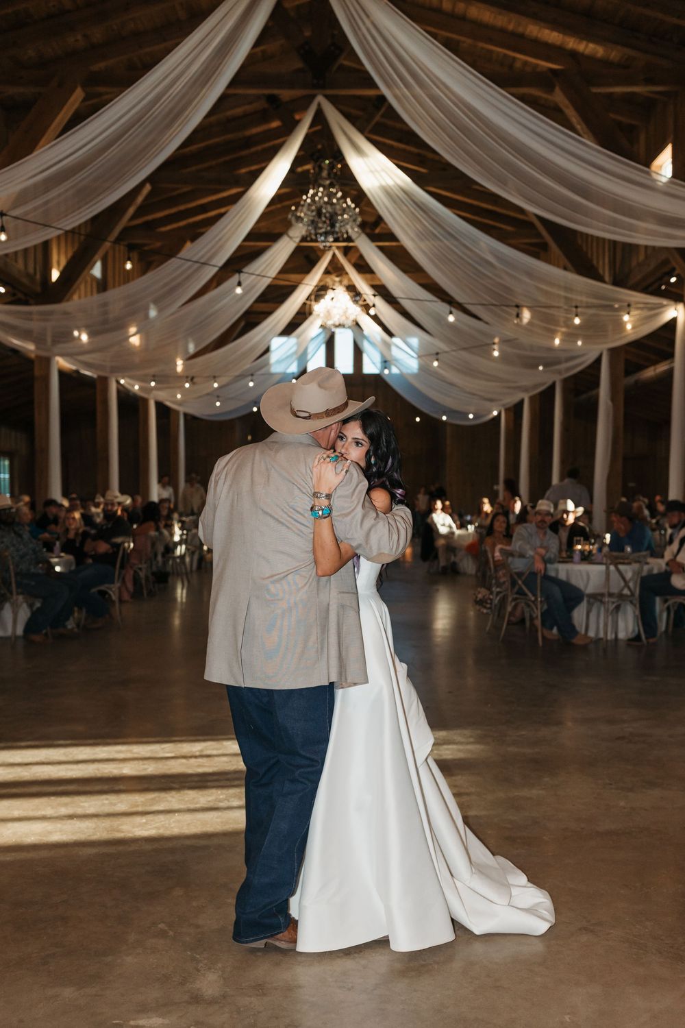 Couples dance beneath elegant white fabric draping and string lights at a rustic barn wedding reception.