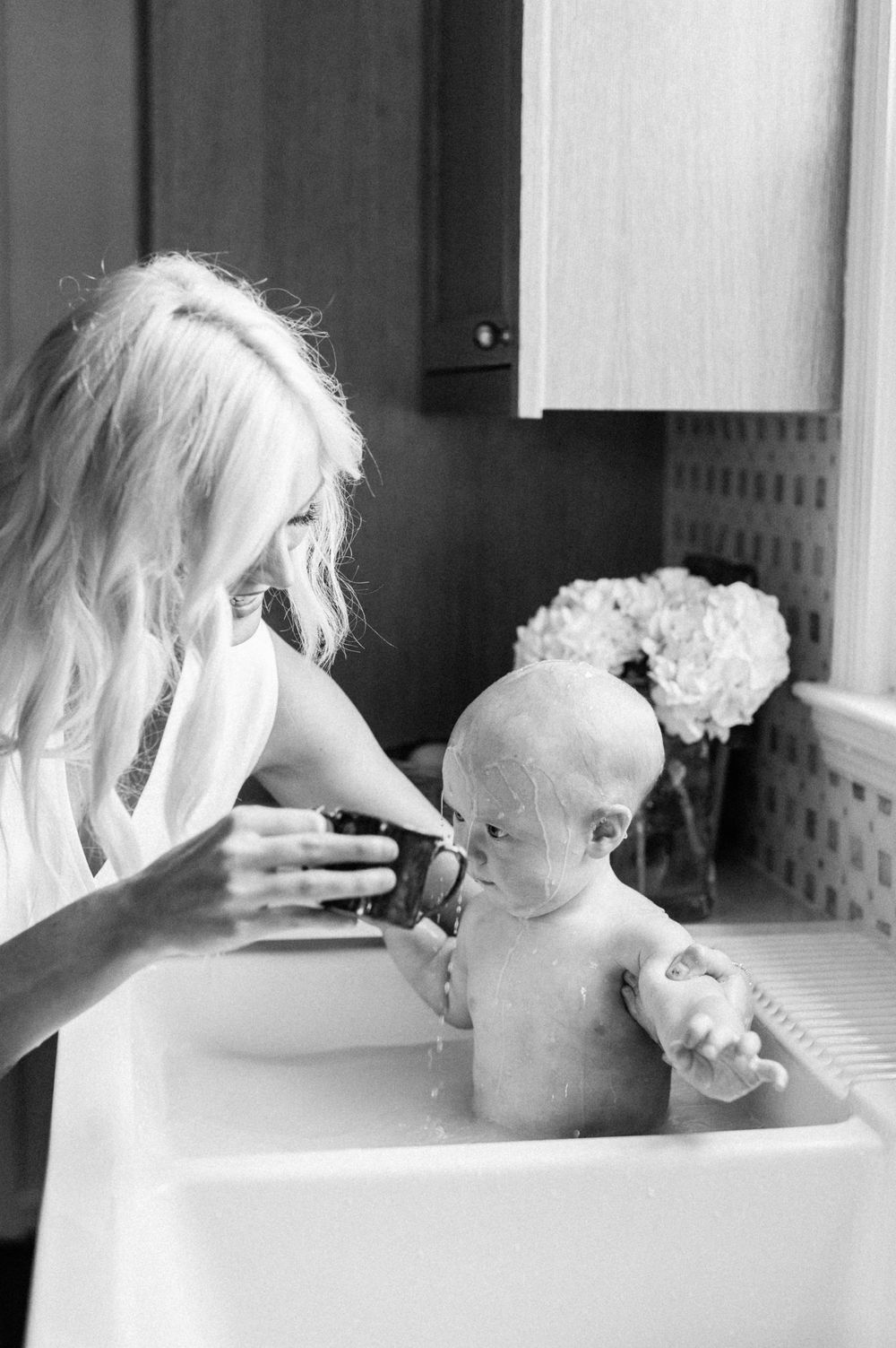 A parent feeding a baby during bath time in a black and white candid photograph series.