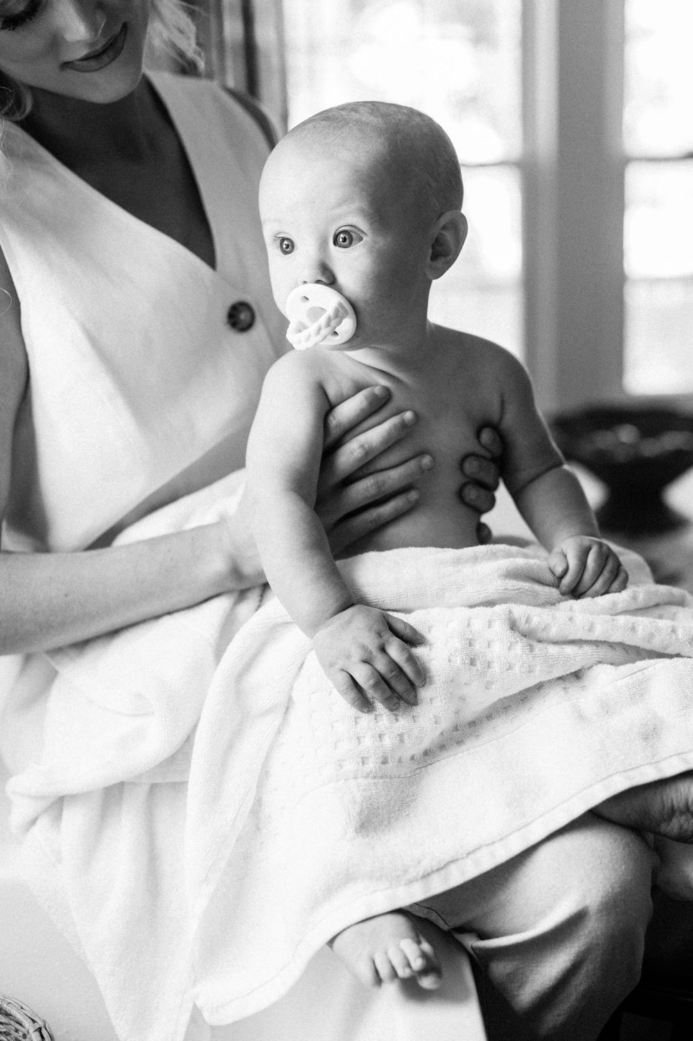 Black and white photo of an infant with a pacifier being held on a white blanket.