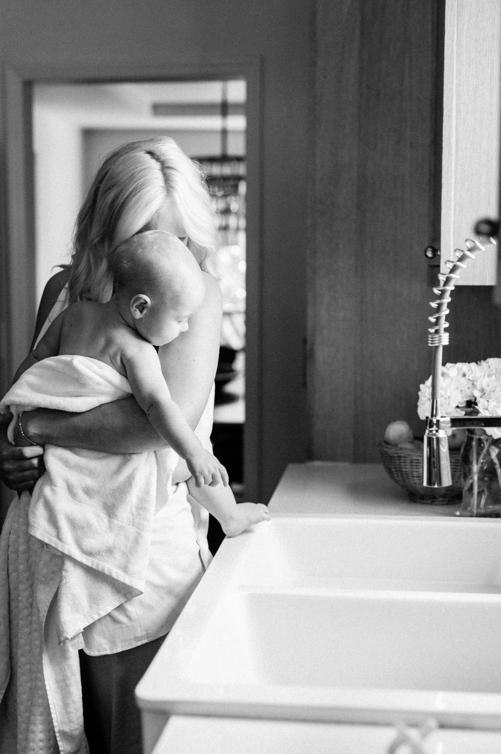 A tender black and white photo of parent and child standing by a large kitchen sink.
