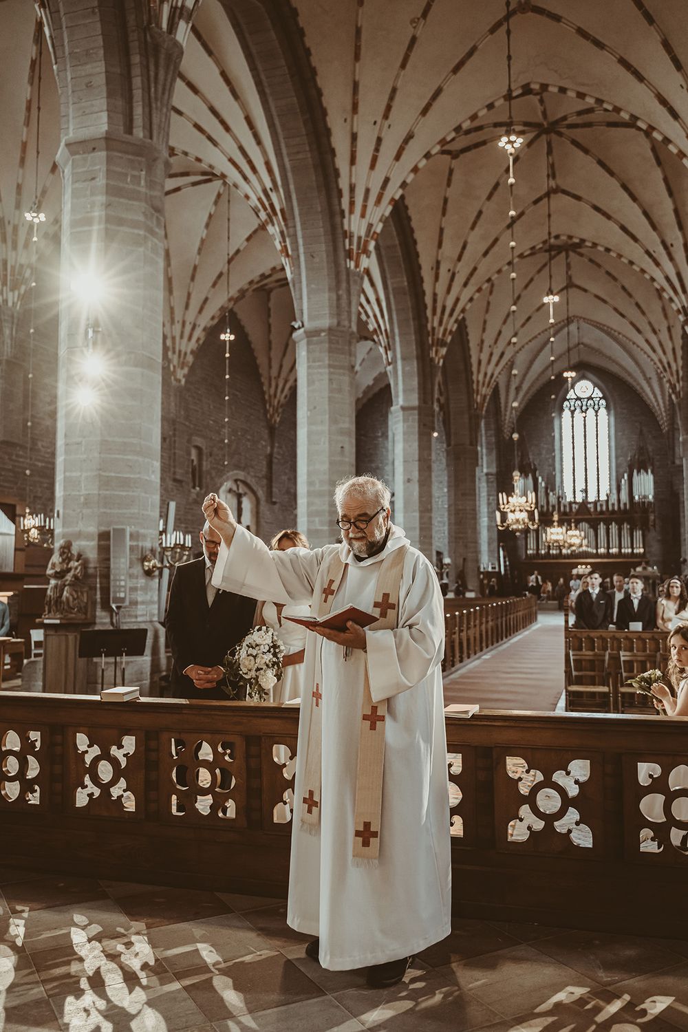 Vigsel i Klosterkyrkan Vadstena, prästen välsignar brudparets ringar. Bröllopsfoto av Lets Bloom Media, bröllopsfotograf Östergötland.