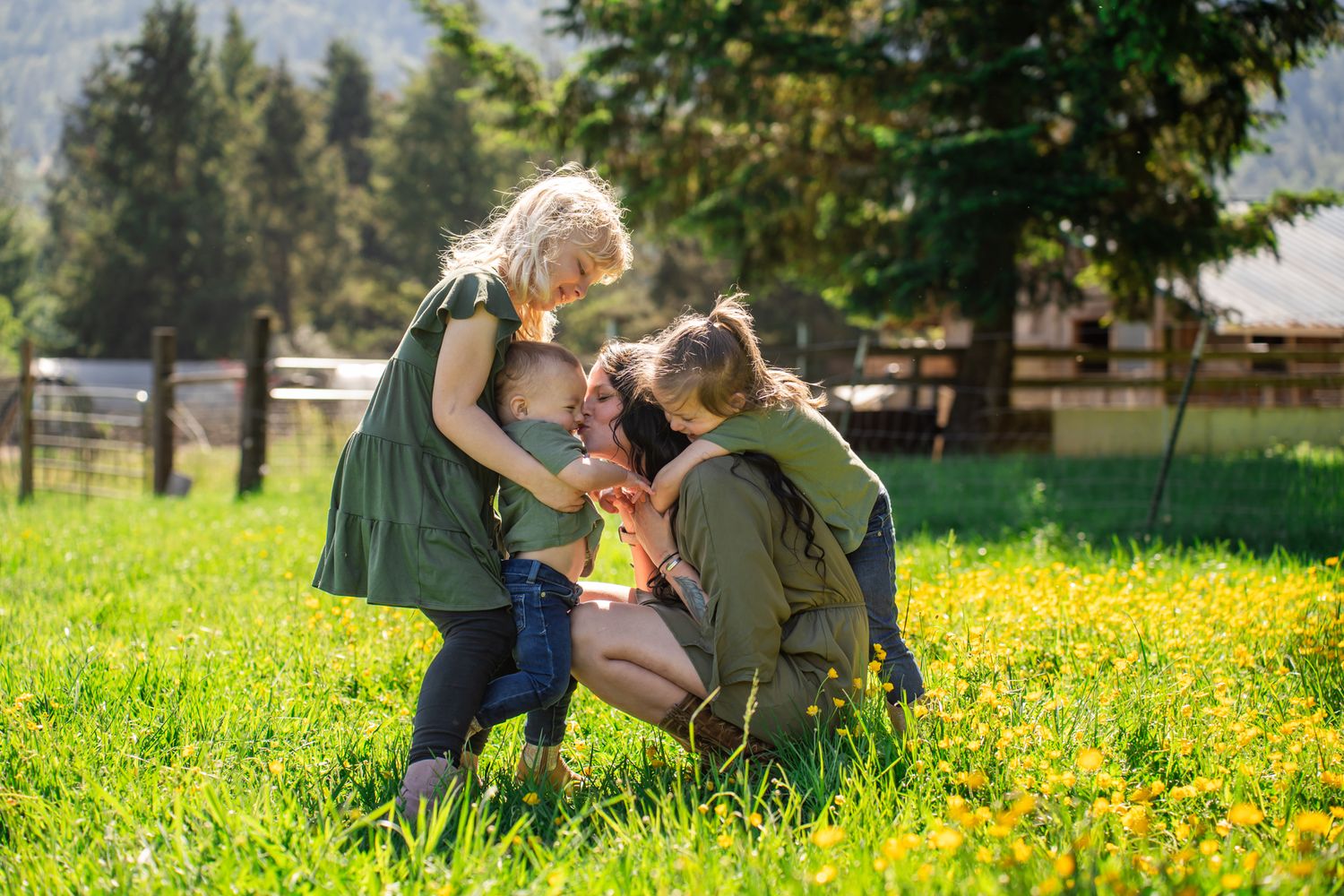 Family Portrait of mom hugging and kissing her 3 daughters in a buttercup field at a farm in Southern Oregon