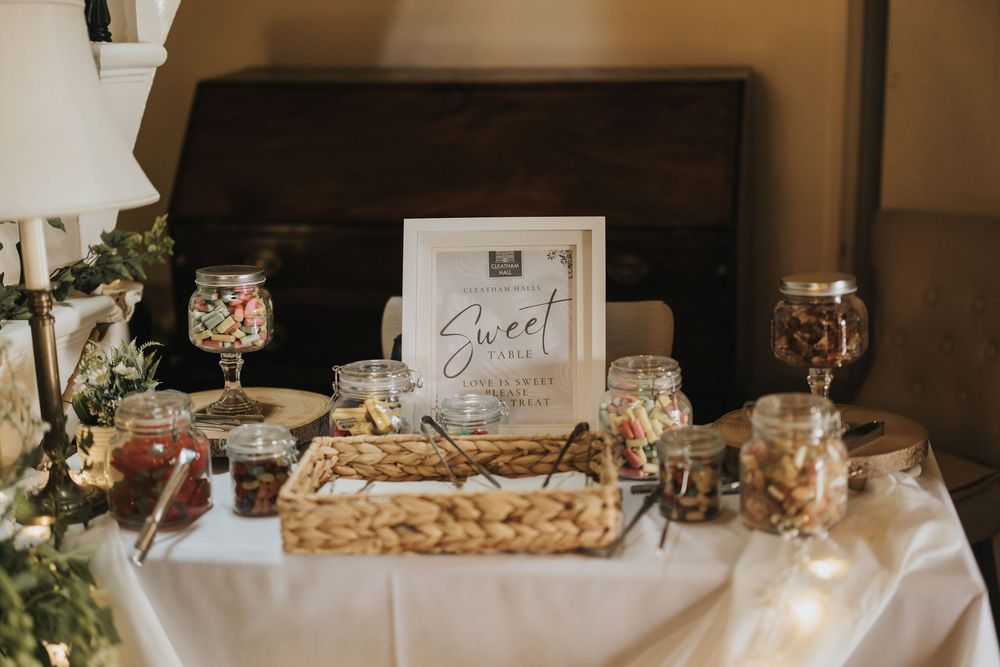 A rustic dessert table with wine glasses, white tablecloth, candle holders and sweet treats for a wedding reception at Cleatham Hall.