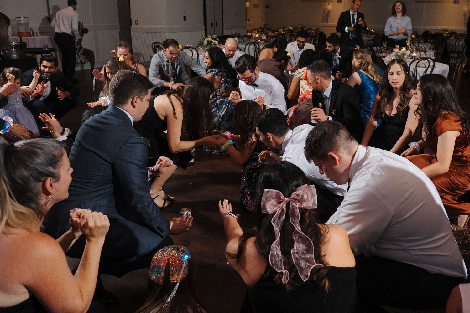Party guests gathered on a dance floor playing a group game at a wedding reception.