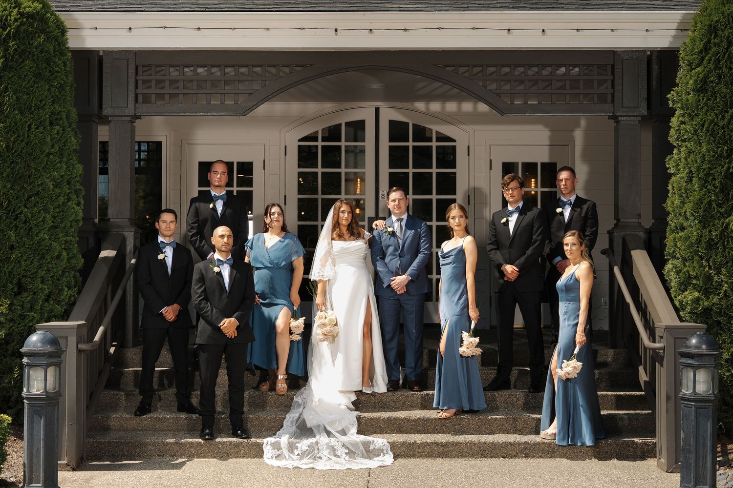 Wedding party gathers for formal portraits on elegant mansion steps during outdoor celebration.