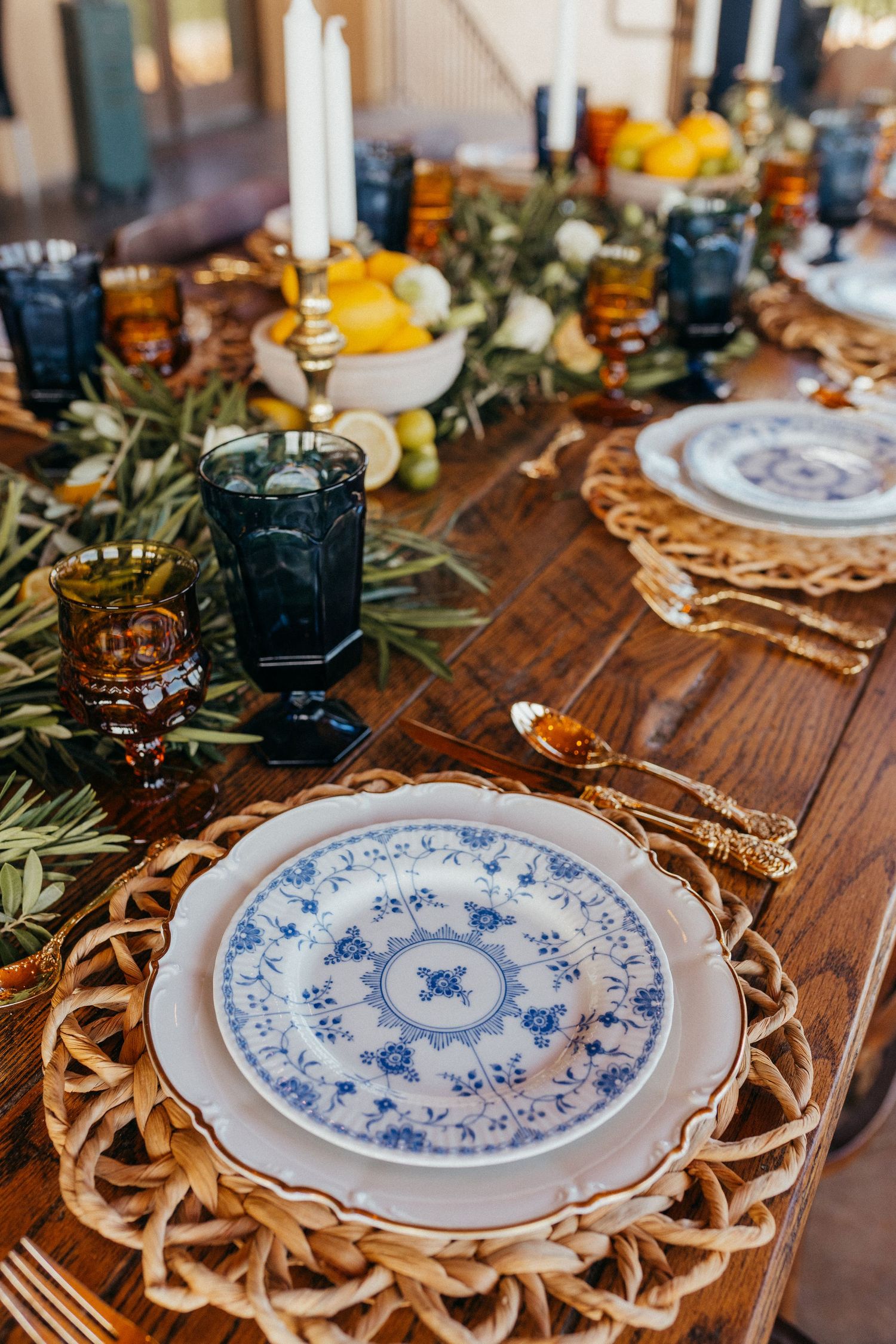 A rustic table setting features vintage blue and white patterned plates on woven rattan chargers with greenery accents.