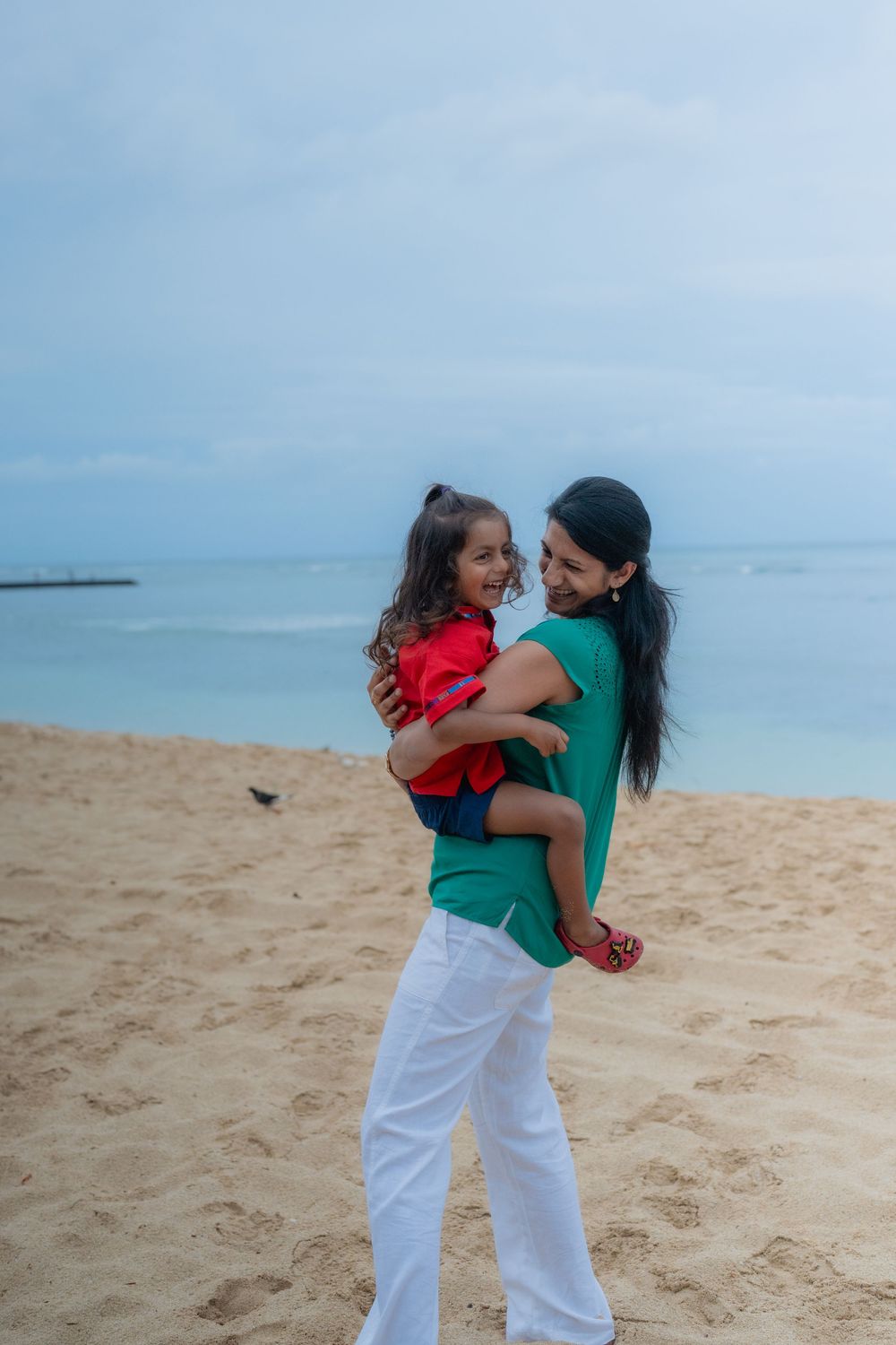 mom spinning young son around on waikiki beach to make him smile for camera