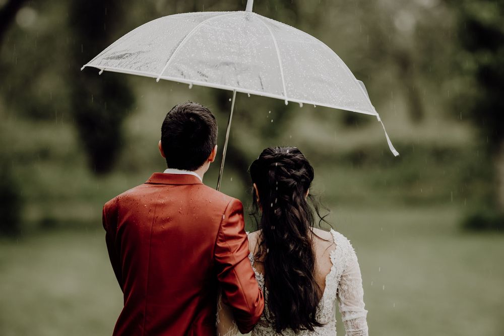Two people stand close together under a white umbrella in a lush garden setting.