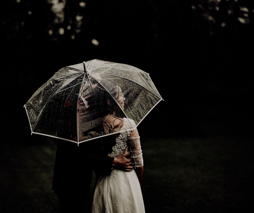 A series of moody, romantic wedding photos showing couples with clear umbrellas in the rain.