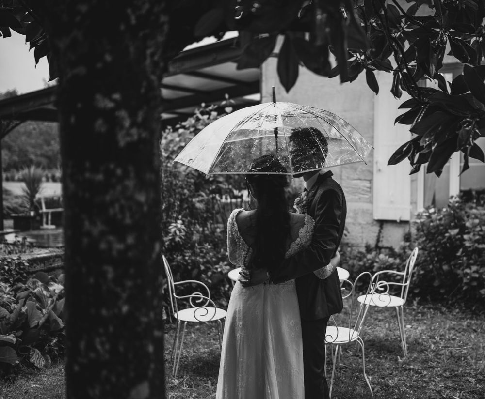 A romantic vintage black and white photograph shows a couple sharing an umbrella in a garden with outdoor seating.