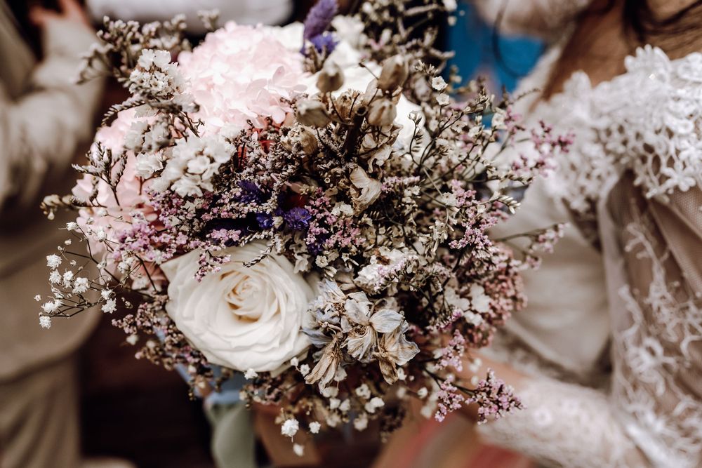 Beautiful wedding bouquet featuring white roses, dried flowers, and baby's breath in soft pink and purple tones.