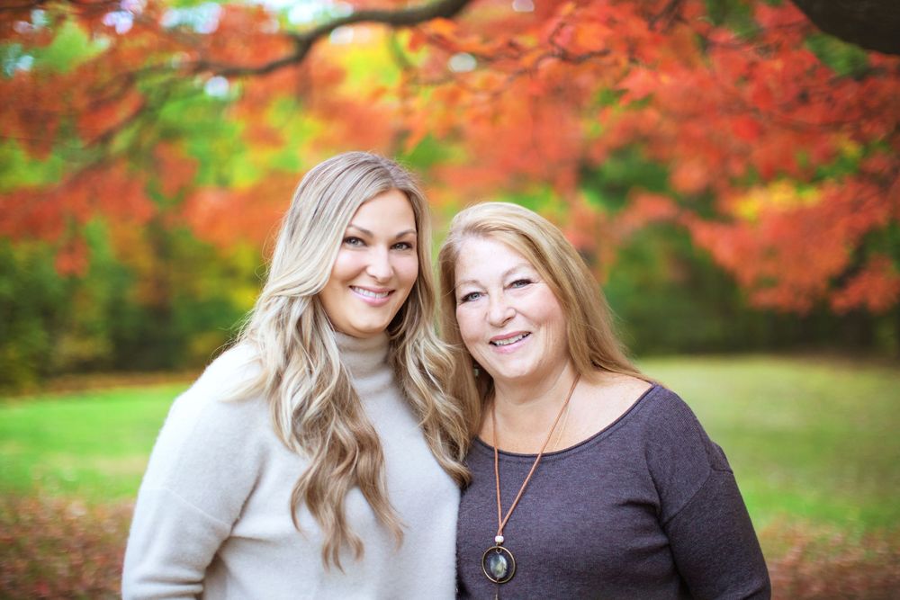 Two people sitting together outdoors with vibrant red autumn foliage in the background during golden hour.