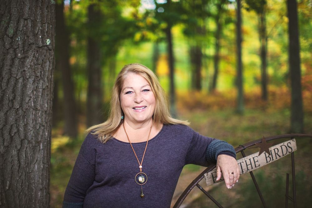 A person wearing a navy blue sweater poses outdoors in front of autumn trees.