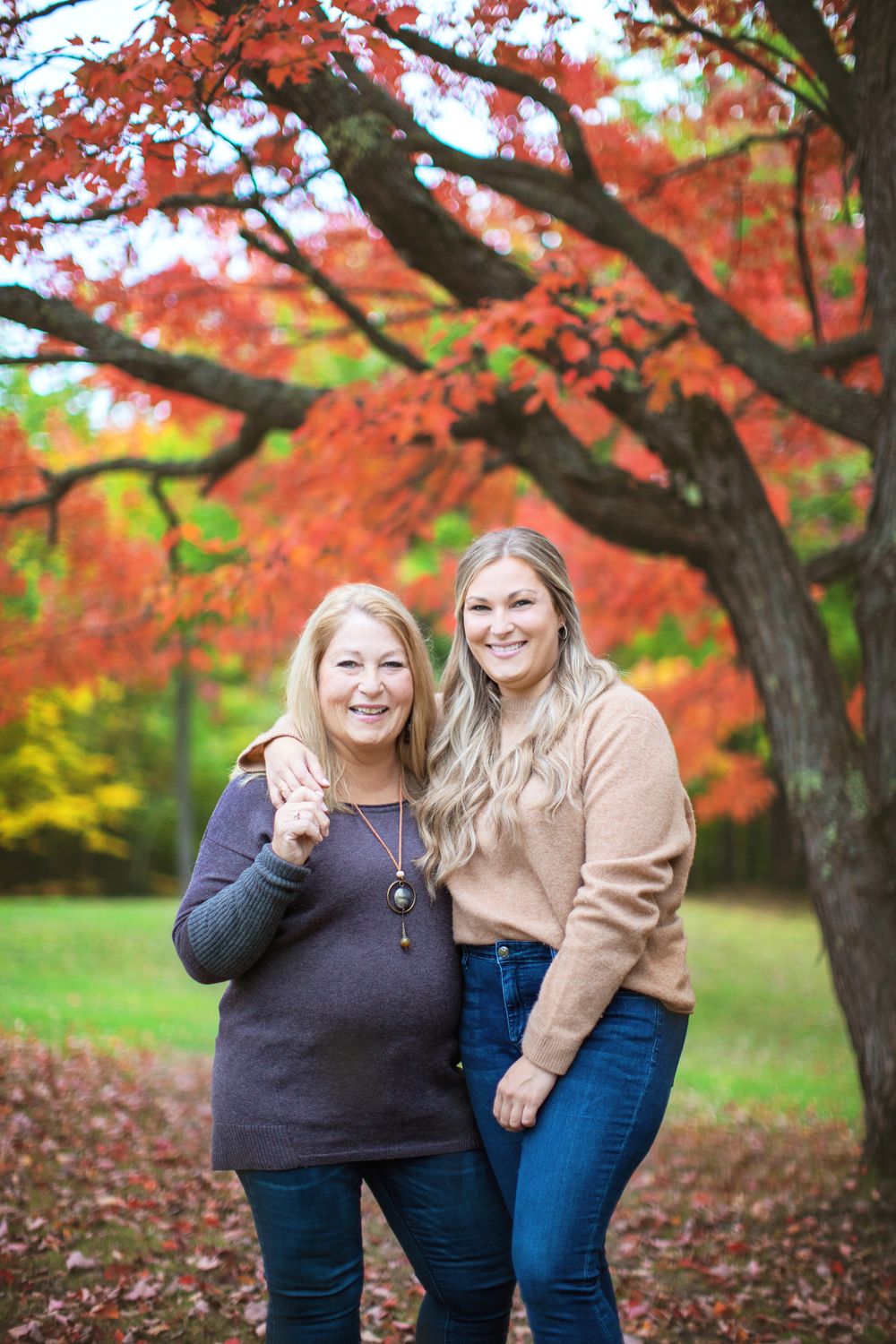Two people share a warm embrace while standing under stunning red maple foliage in an autumn park setting.