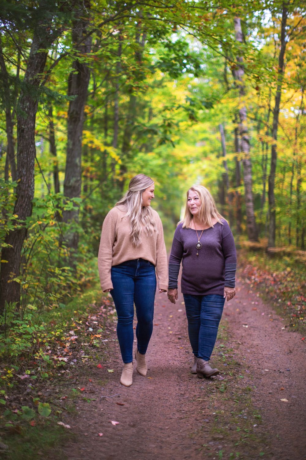 Two people stroll together along a forest path surrounded by vibrant fall colors.