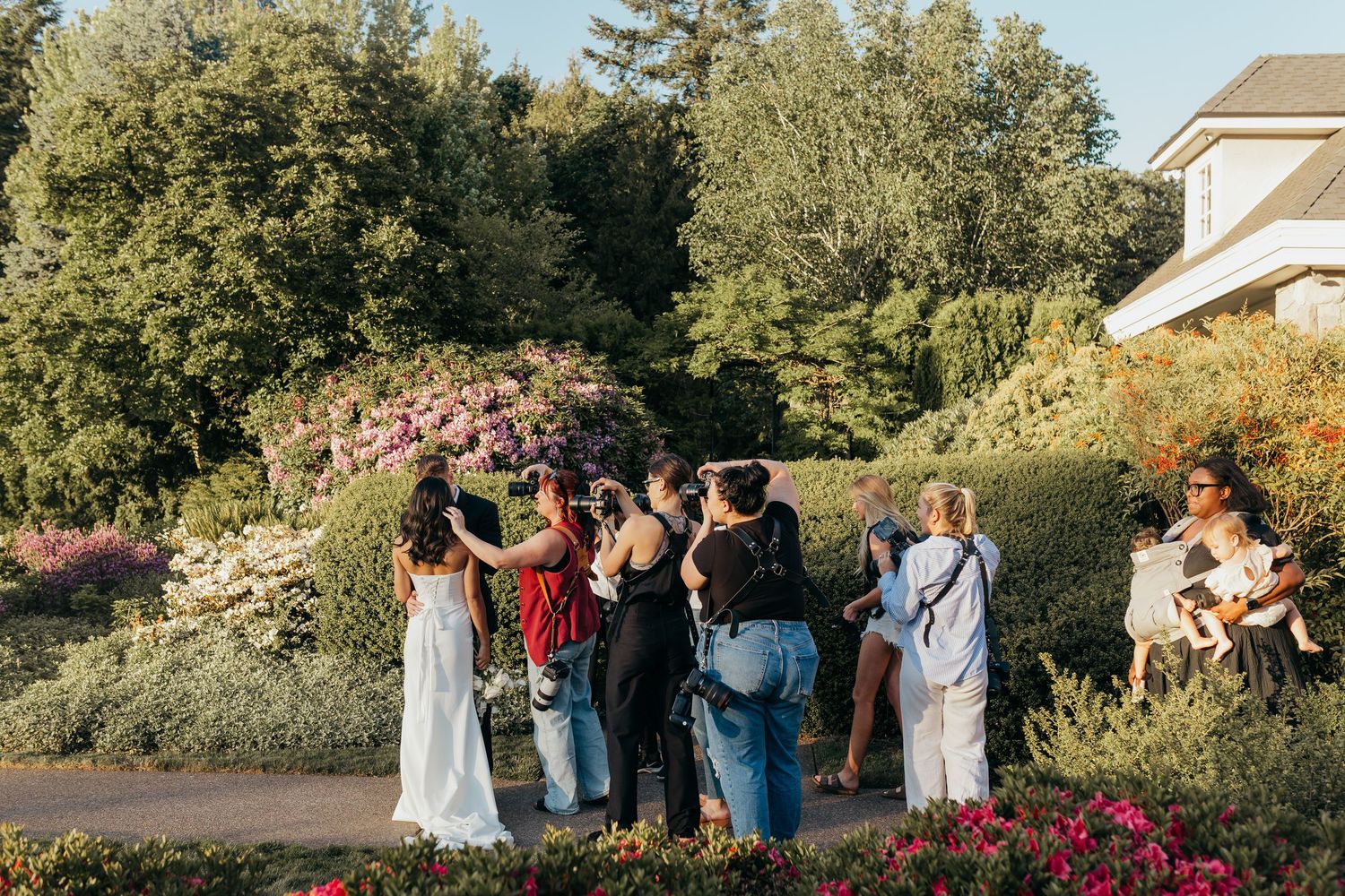 Guests gather outside for a sunset wedding ceremony surrounded by lush gardens and blooming pink flowers.
