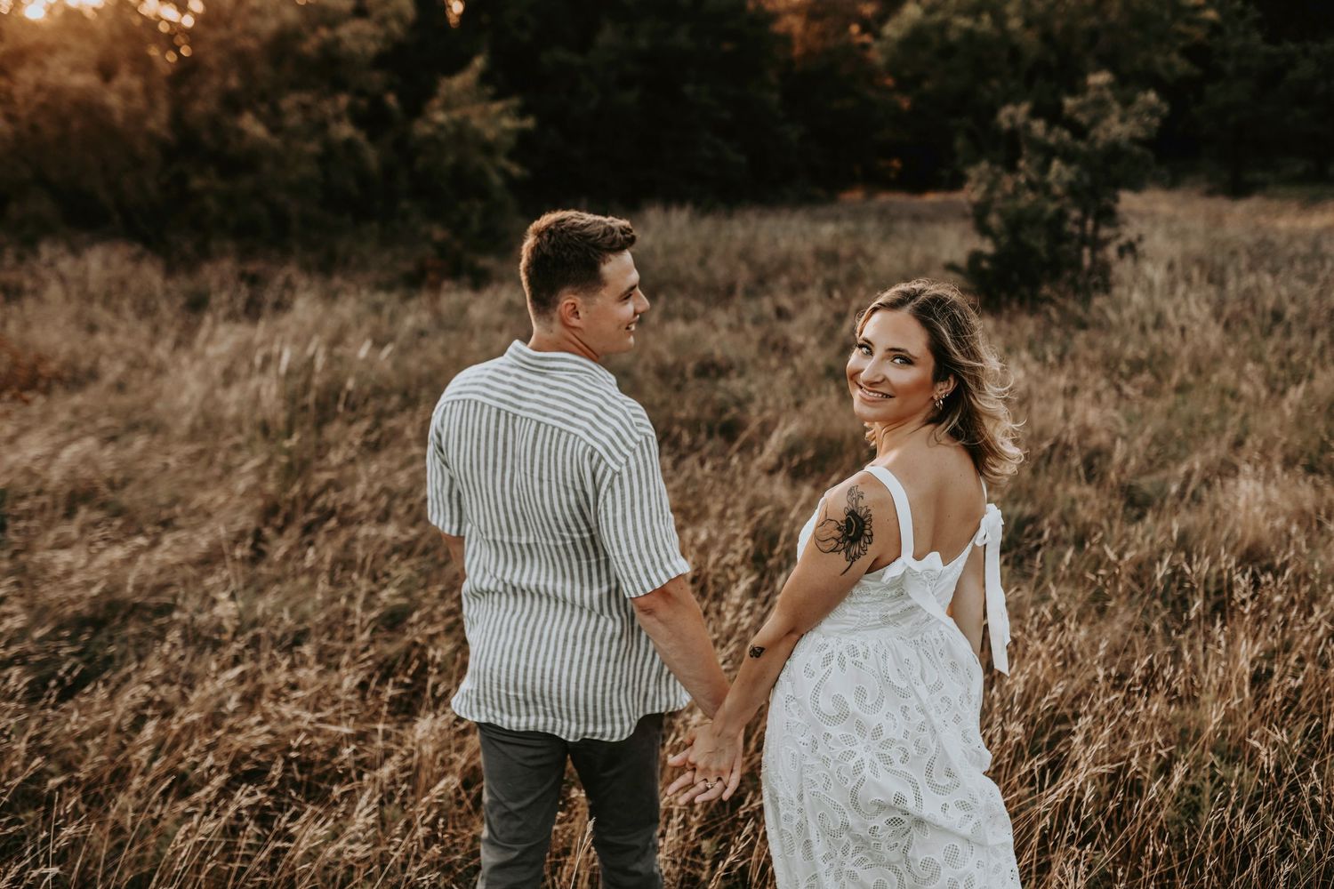 Couple holding hands and walking through tall grass during sunset engagement session